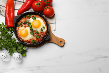 Flat lay composition with delicious shakshuka in frying pan on white marble table. Space for text
