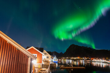 beautiful northern lights over Sørvågen village with red fisherman cabins on shore of lofoten islands