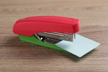 One new bright stapler with paper note on wooden table, closeup