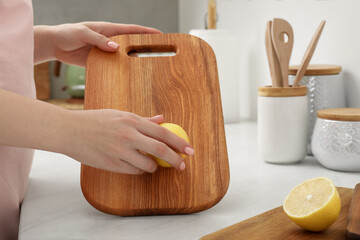 Woman rubbing wooden cutting board with lemon at white table in kitchen, closeup - obrazy, fototapety, plakaty