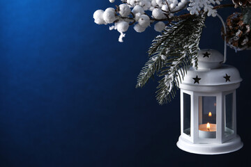 Christmas lantern with burning candle on fir tree against blue background, closeup. Space for text