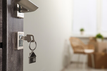 Mortgage and real estate. Open door with key and house shaped keychain against blurred background,...