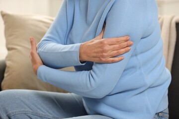 Mature woman suffering from pain in arm indoors, closeup. Rheumatism symptom