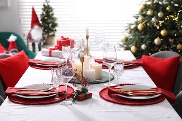 Christmas table setting with burning candles, gift box and dishware indoors