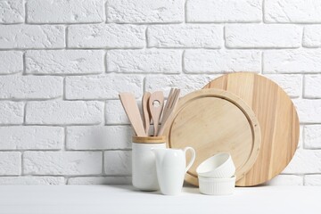 Cutting boards, kitchen utensils and dishware on white table near brick wall. Space for text