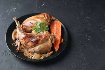 Tasty cooked rabbit meat with vegetables and parsley on black table, space for text - obrazy, fototapety, plakaty