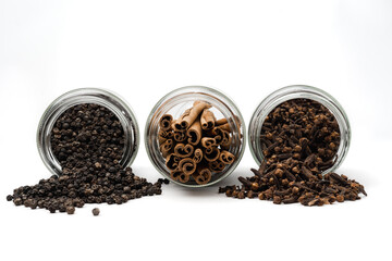 spill out spices from glass jar, black peppercorn, cinnamon and cloves, isolated on white...