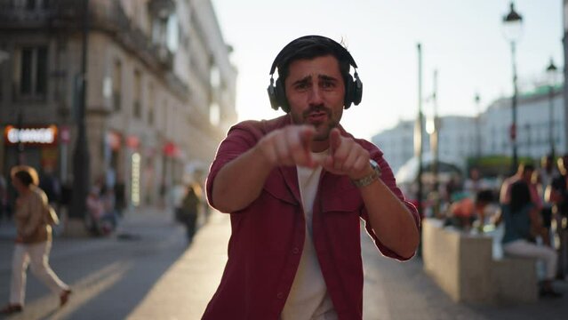 Joyful young adult man with headphones dancing in the street, enjoying music. Casual urban life scene with blurred city background in daylight