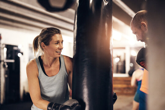 Mature woman holding a boxing gym punching bag for her partner