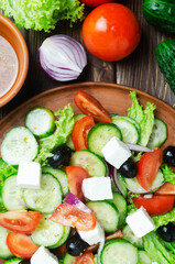 Classic Greek salad with cucumbers, tomatoes, red onion, feta cheese, lettuce and black olives on a wooden table. The concept of traditional dishes. Bossage. Simple ingredients. Top view.