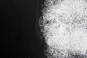 Wheat flour is scattered in a thin layer on a black background.