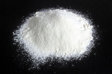 A pile of white crumbly flour lies on a black background