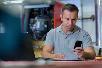 man in industrial setting with laptop and smartphone