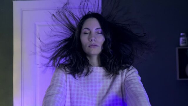 Portrait of a young sleepwalking woman in pajamas slowly raising her hands in front of her at night in a room. Her hair is flying in the air. The concept of somnambulism