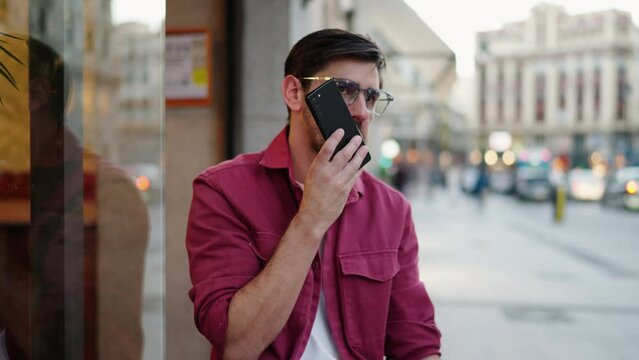 Smart Man in red shirt records audio message on mobile phone, modern multitasking tool for task management. urban street scene reflects dynamic life where business and technology intersect on the go