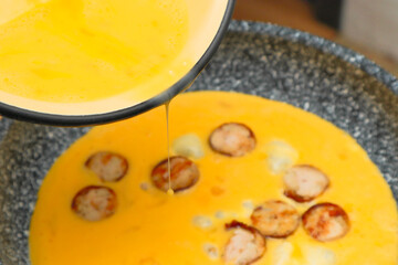Cooking omelette with sausage. Liquid egg for scrambled eggs with is being poured into frying pan.