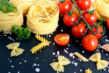Pasta in the shape of a nest and tomatoes lie on a black stone background.