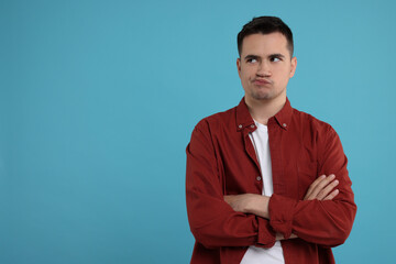 Resentful man with crossed arms on light blue background, space for text