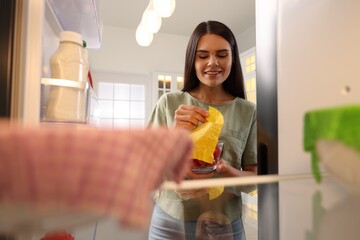 Happy woman taking away beeswax food wrap, view from refrigerator - obrazy, fototapety, plakaty