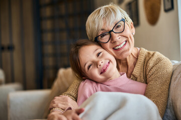Portrait of a grandma and her grandchild, sitting on the couch, in a hug, covered in a blanket.