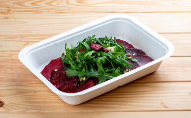 Beet carpaccio, arugula and nuts. Vegetarian food. Takeaway food. On a wooden background.
