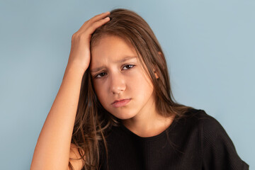 Little tired exhausted kid teen girl of 10 years old in black T-shirt put hand on forehead. look camera on pastel plain light blue background..
