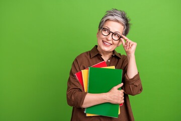 Photo of intelligent woman with short haircut touch glasses hold copybooks look at promo empty space isolated on green color background