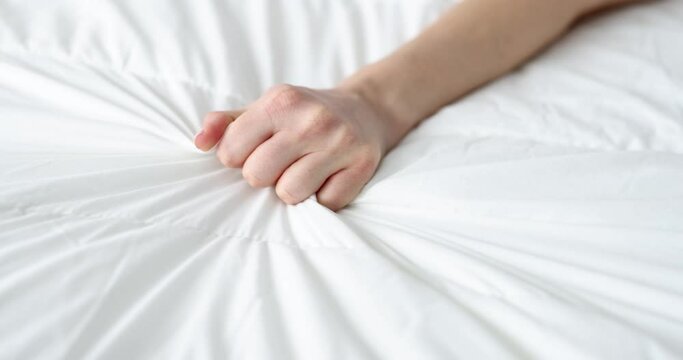 Woman's hand squeezing sheet on the bed, close-up, slow motion. Hand grabs a white crumpled blanket