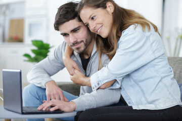 couple embracing while looking at laptop together - obrazy, fototapety, plakaty
