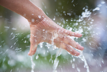 A woman's hand under splashes of water from a fountain. - obrazy, fototapety, plakaty
