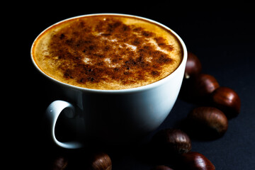 Cup of coffee with cinnamon, surrounded by chestnuts, during winter and holiday season