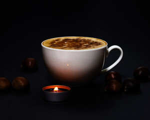 Cup of coffee with cinnamon, surrounded by chestnuts and a small perfumed candle, during winter and holiday season, bright and dark contrast, chiaroscuro