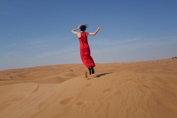 Fototapeta na wymiar Woman in red dress on sand dunes