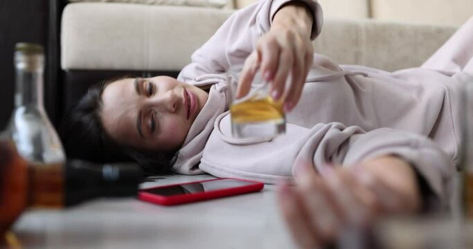 A drunk woman on the couch holds out her hand to a glass of alcohol. Hangover syndrome, female alcoholism