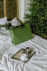 Breakfast in a bed. Christmas tree lights. Gift in a green box. Excellent morning. Happy New year with a cup of coffee. Beautiful interior in a room.