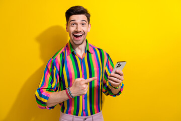 Photo of surprised guy wearing striped shirt point finger his new smartphone which works much...