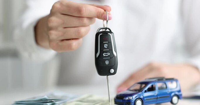 A woman holds a car key, money is on the table, close-up, slow motion. Purchase of a vehicle, insurance