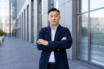 Portrait of a young Asian male lawyer, businessman standing outside an office building in a suit,...