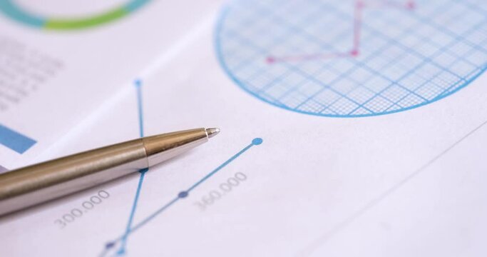 A silver stylish pen lies on the charts, close-up. The concept of financial analysis, the workplace of the manager, the change in indicators
