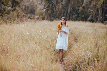 Young Caucasian woman walking in a field and holding a bouquet of sunflowers. Romantic woman...