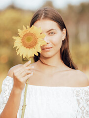 Close up portrait of charming woman holding sunflower. One eye is covered by sunflower. Nature and outdoor concept. Summer time. Beautiful face. Romantic mood.
