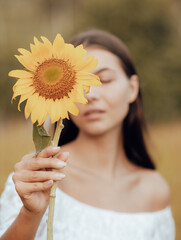 Close up portrait of charming woman holding sunflower. One eye is covered by sunflower. Focus on the fower. Blurred face and body. Nature and outdoor concept. Summer time.