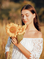 Close up portrait of attractive woman holding sunflowers. Nature and outdoor concept. Summer time. Beautiful face. Closed eyes. Sunset time.