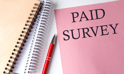 PAID SURVEY word on the pink paper with office tools on white background