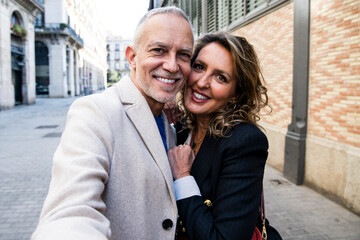 Active mid adult couple taking selfie together on the street looking at camera. Lovely happy mature man and woman having fun together taking a photo in weekend trip.