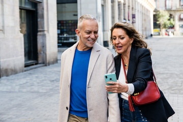 Married middle aged man and woman looking for touristic location checking map in their smartphone. Happy senior man with his wife using phone together standing in the street.