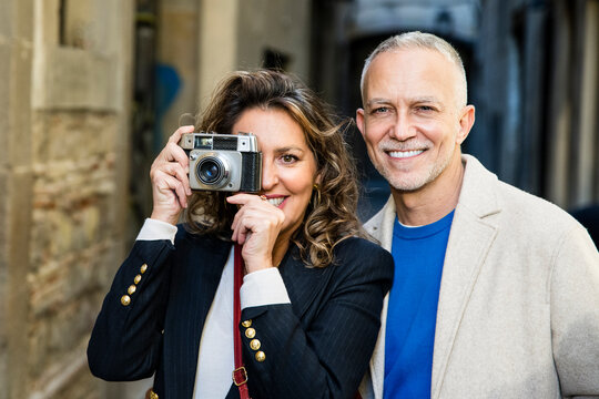 Mid adult tourist couple taking picture on vintage camera looking at camera. Senior woman taking photography in a city street with her husband.