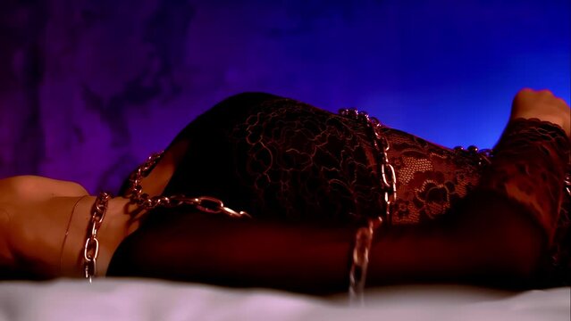 BDSM fetish concept, sexy girl in erotic lingerie tied up with metal chains lying on bed, temptation. Hot passionate sensual woman. Intimate adult games with punishment. Caucasian brunette young lady