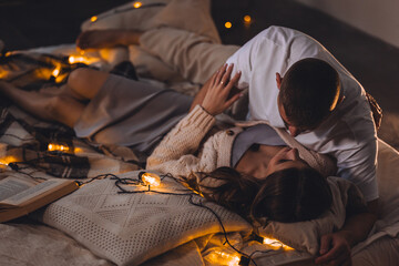 Beautiful happy loving young smiling couple relaxing in bed, watching movies on projector. Cozy...