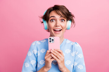 Photo of astonished cheerful lady open mouth hold smart phone listen music headphones isolated on...